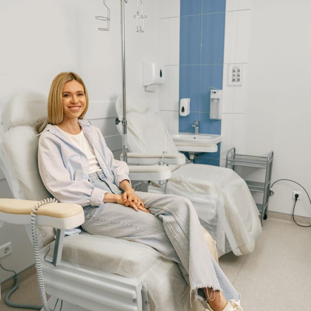 Smiling woman sitting in armchair while waiting for IV infusion during treatment in hospital