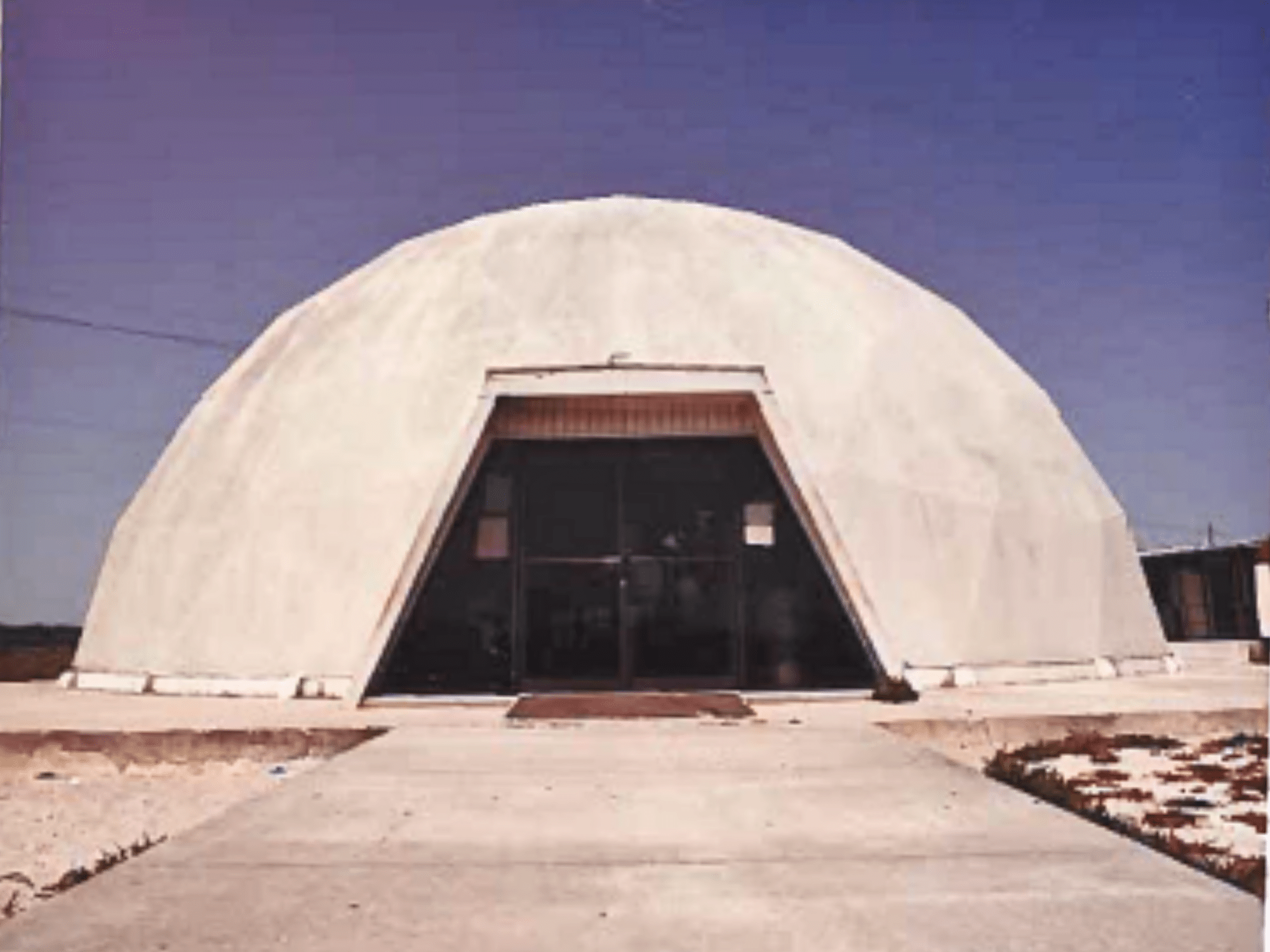 A white dome or igloo shaped building with an trapezoid shaped door.